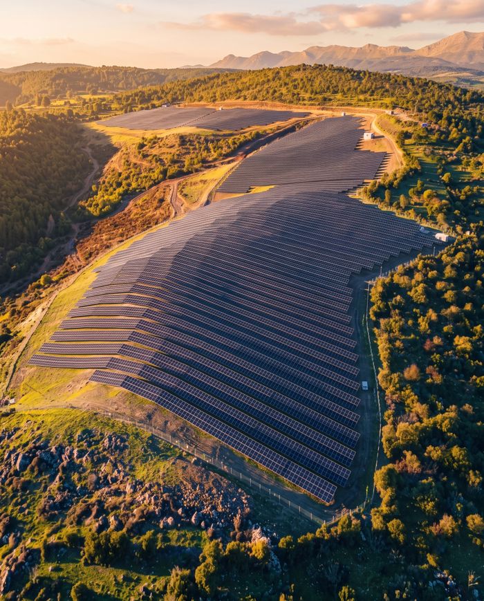 about-us Aerial view of a vast solar panel installation amidst a hilly landscape under a beautiful sunset.