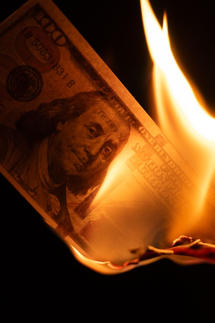A US $100 bill igniting in flames, symbolizing financial crises or economic instability.