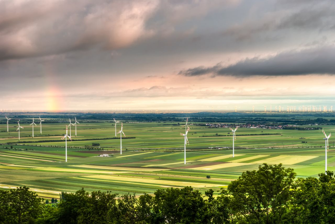 Beautiful aerial view of a wind farm in a lush countryside with a rainbow on the horizon, showcasing renewable energy and nature.